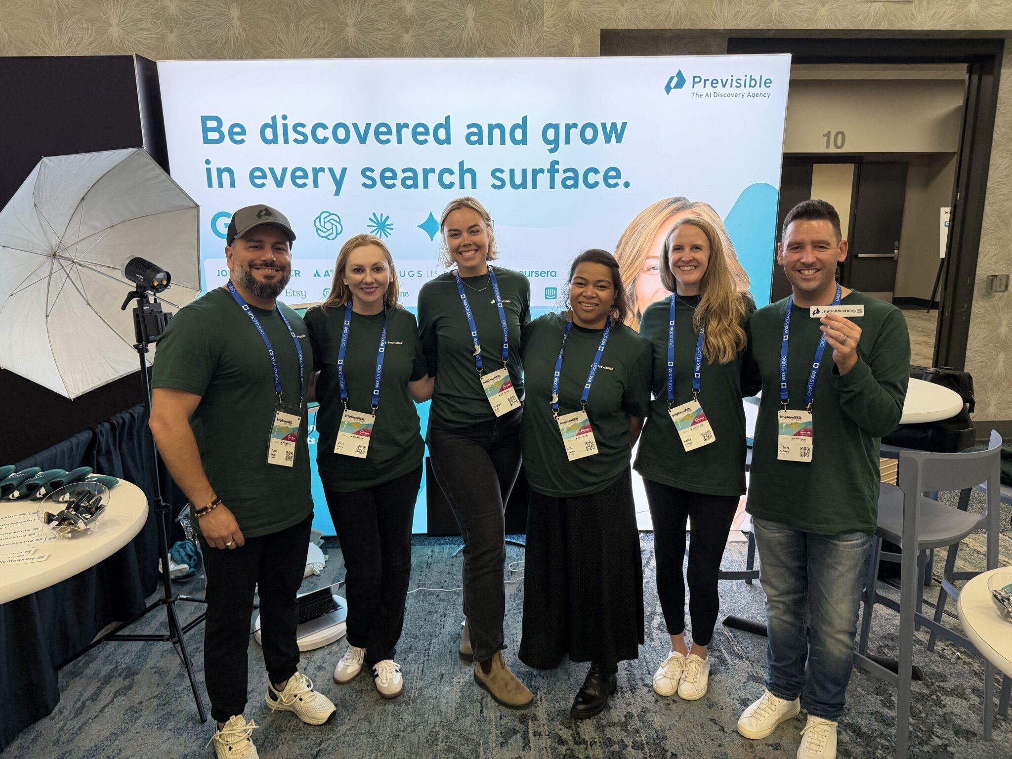 Six smiling people in green shirts pose in front of a “Previsible” booth at a conference, sharing their excitement and highlights from the event in this brightonseo recap.